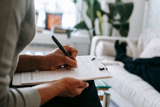 A therapist sitting next to a patient while writing on a clipboard